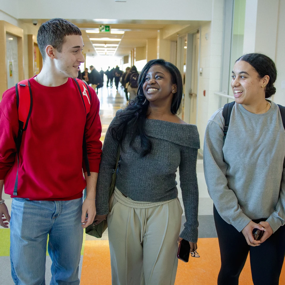 trois élèves dans le couloir d'une école secondaire, qui se regardent souriant