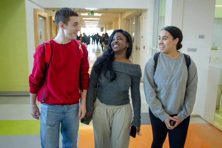 trois élèves dans le couloir d'une école secondaire, qui se regardent souriant