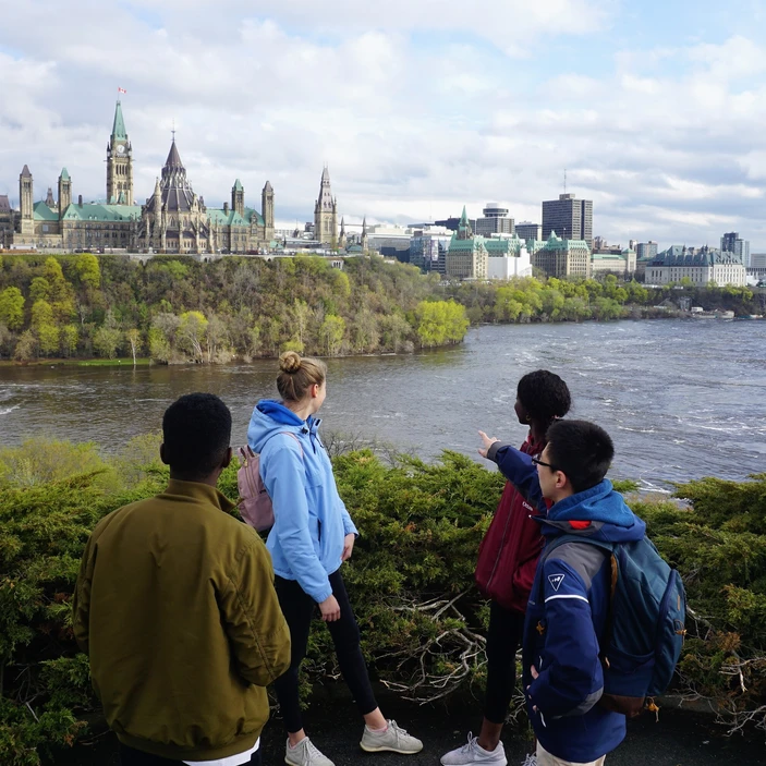 Un groupe de jeunes regardent la ville d'Ottawa situé de l'autre côté de la rivière des Outaouais. L'un d'entre eux pointe vers le parlement.